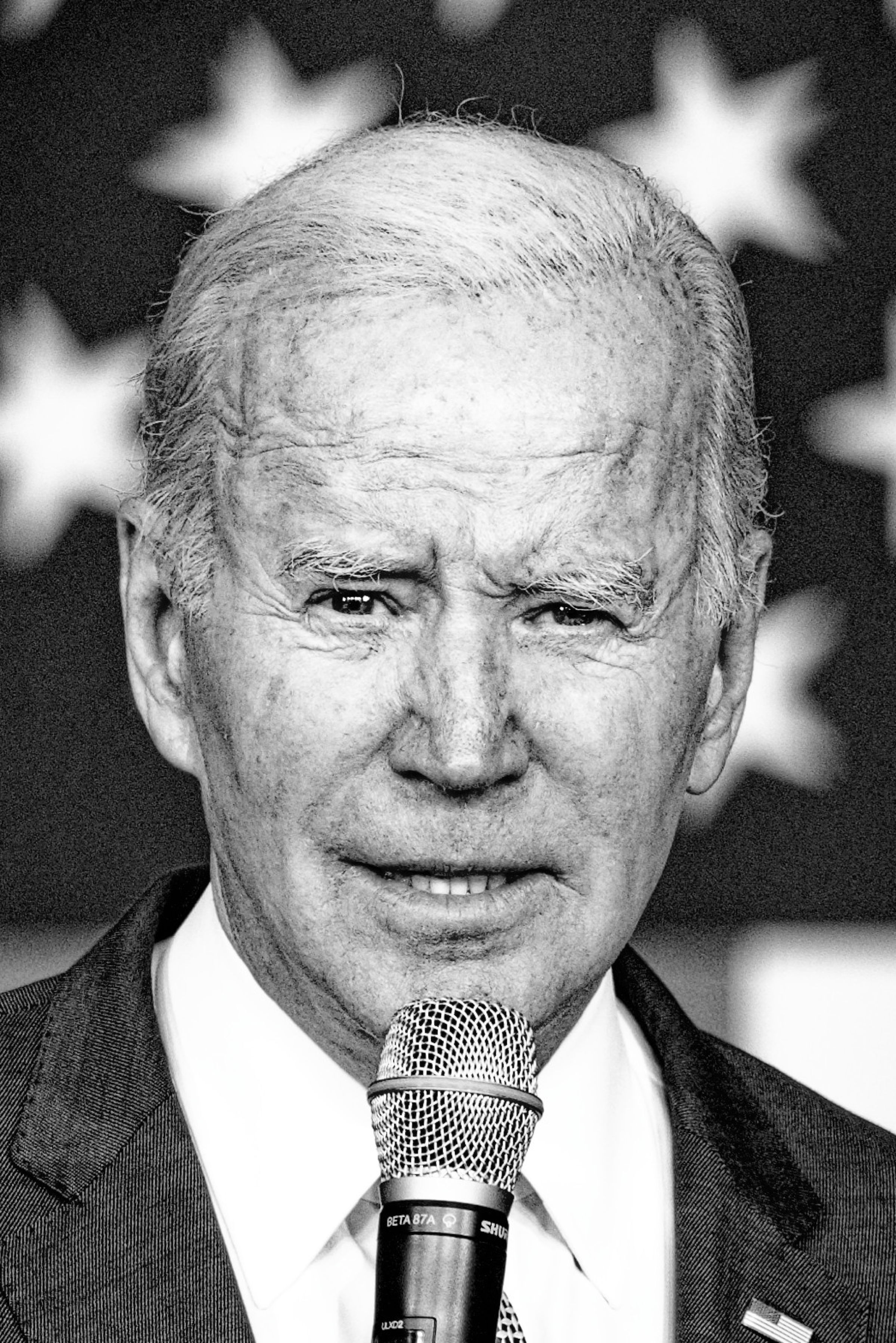 A black and white close-up portrait of President Joe Biden speaking into a microphone. His face shows detailed wrinkles and a slight smile, with stars from the American flag visible behind him.