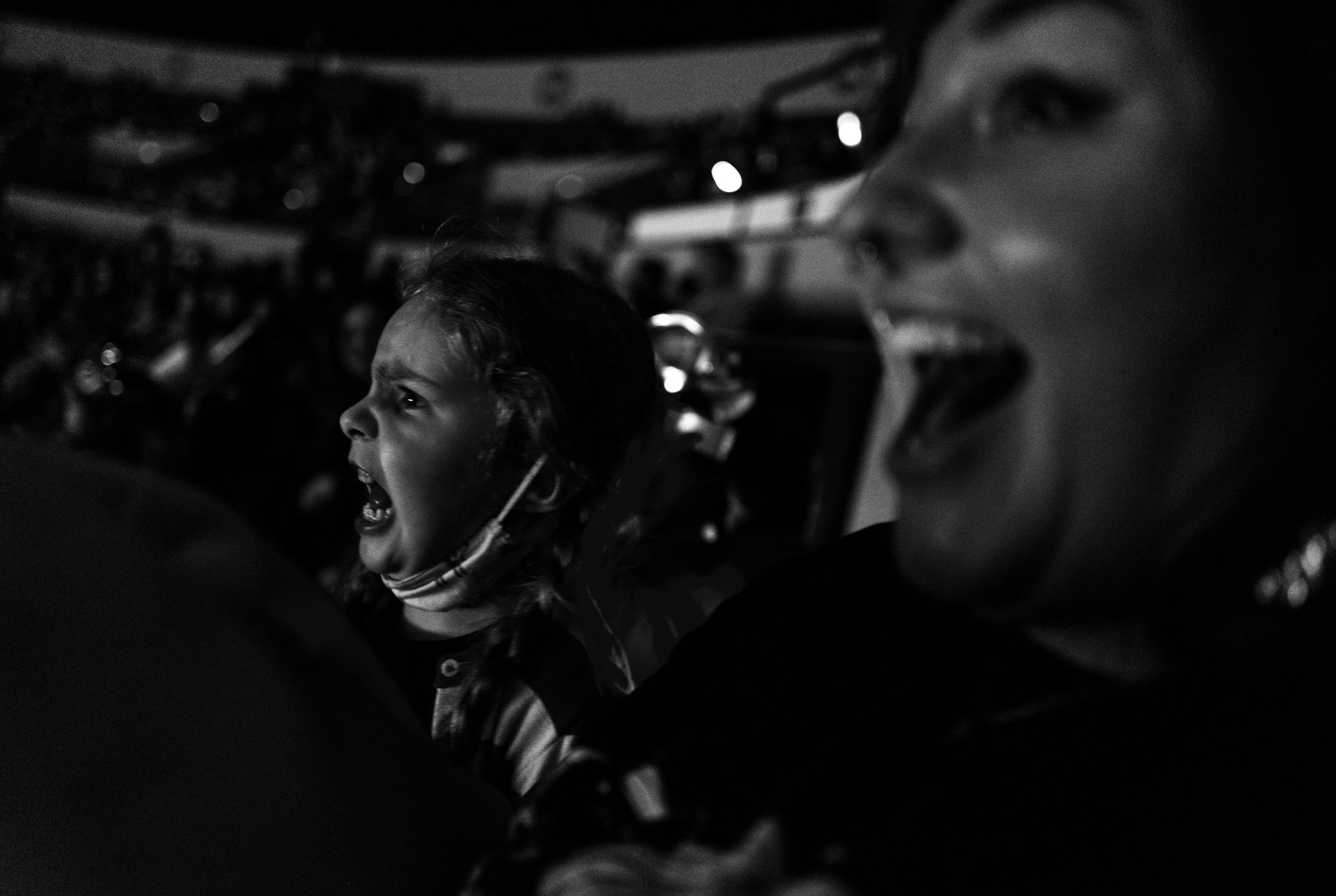 Two people, a young girl and an adult woman, shouting excitedly in a dark venue, their faces lit dramatically.