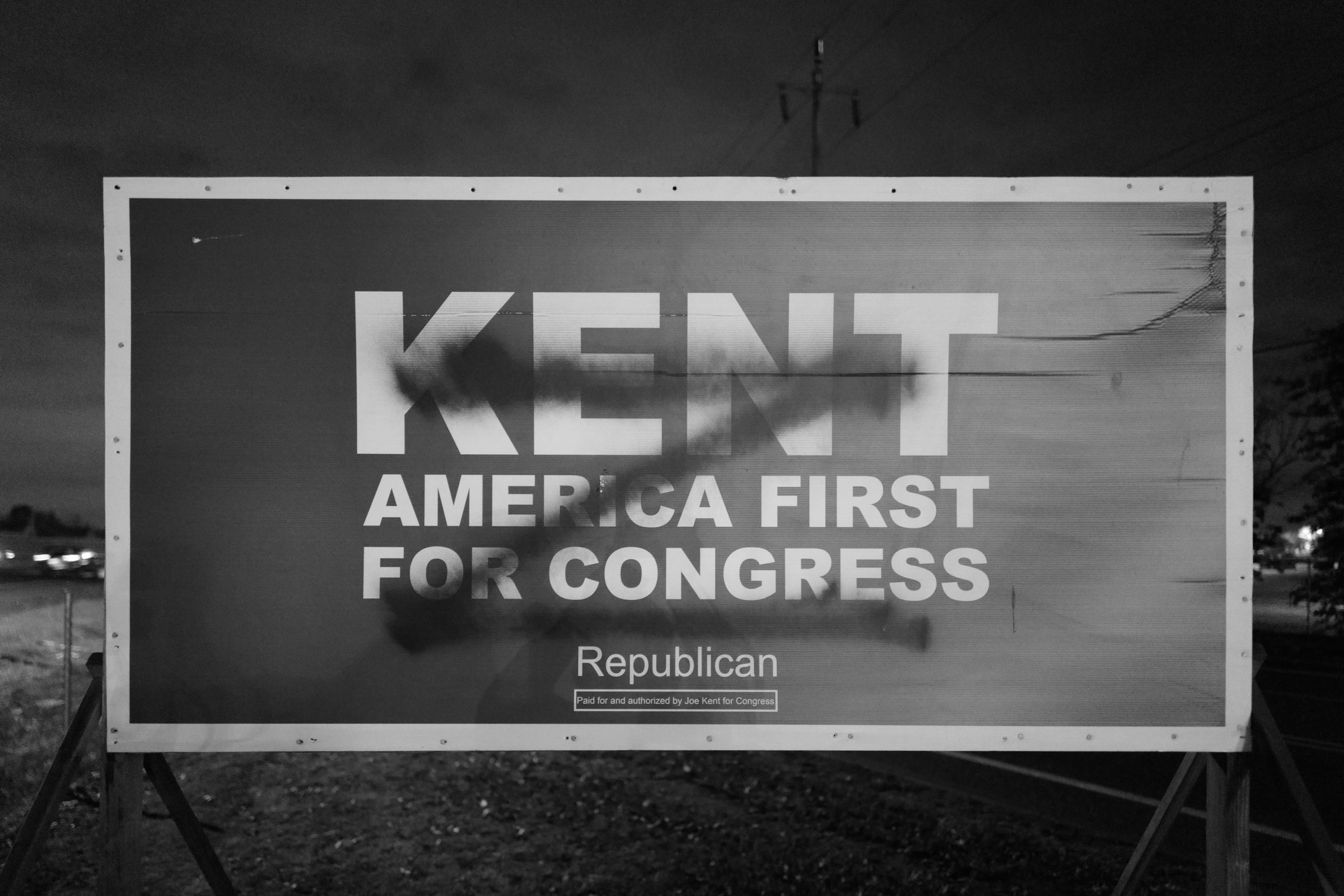 A vandalized "KENT AMERICA FIRST FOR CONGRESS" campaign sign with the name partially obscured by dark spray paint. A single letter "Z" is spray painted on top of Kent's name and slogan. The letter “Z” was a symbol displayed on Russian military vehicles during the 2022 invasion of Ukraine and in Russian propaganda. Kent and his supporters had previously faced backlash from the local Ukrainian community over support for Russia.